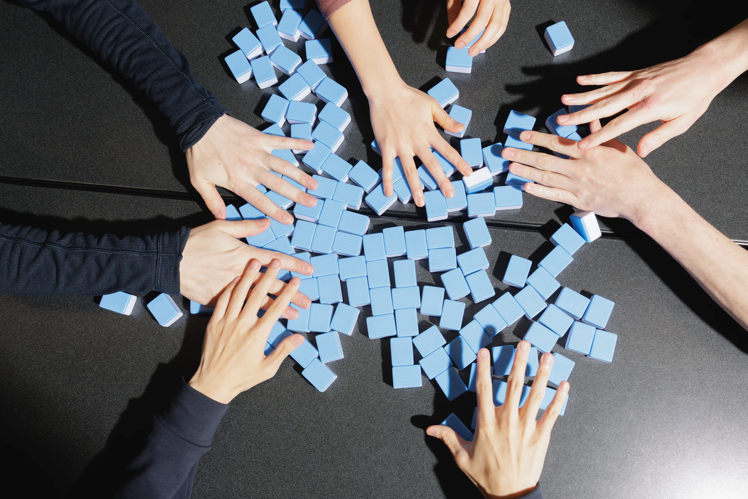 Hands washing mahjong tiles at a table.