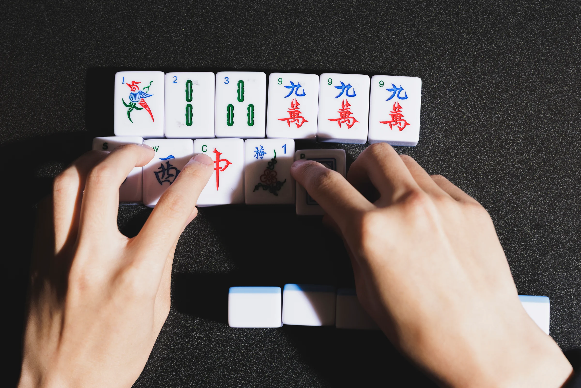 A hand of mahjong tiles being arranged on a table.
